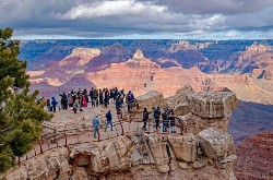 A ground of tourists stand on a gated cliffside overlooking the canyon.